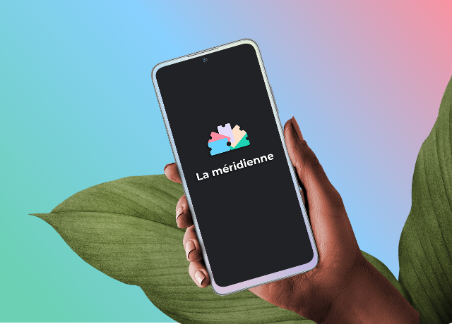 Image d'une main qui tient un smartphone sur lequel on voit affiché le logo de La pause méridienne. Il y a également deux feuilles d'une plante en fond, ainsi qu'un dégradé de couleur en arrière plan